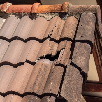 Severe storm and wind damage with missing and displaced roof tiles on a house